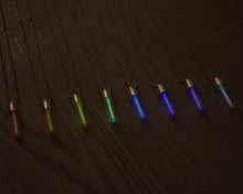 Load image into Gallery viewer, Tritium glow in the dark rainbow glass vial pendants. Picture shows red, orange yellow, green, light blue, dark blue, purple and white necklaces with silver coloured caps and stainless steel ball chain.