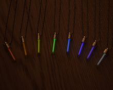 Load image into Gallery viewer, Tritium glow in the dark rainbow glass vial pendants. Picture shows red, orange yellow, green, light blue, dark blue, purple and white necklaces with silver coloured caps and stainless steel ball chain.